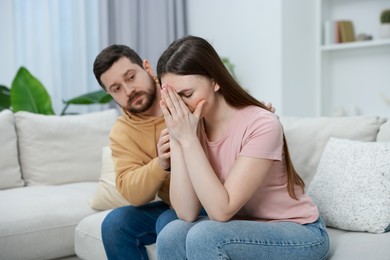 Photo of Man comforting his resentful girlfriend on couch at home, selective focus