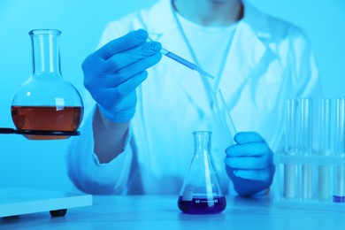 Photo of Laboratory testing. Scientist working with glassware at table, closeup. Toned in blue