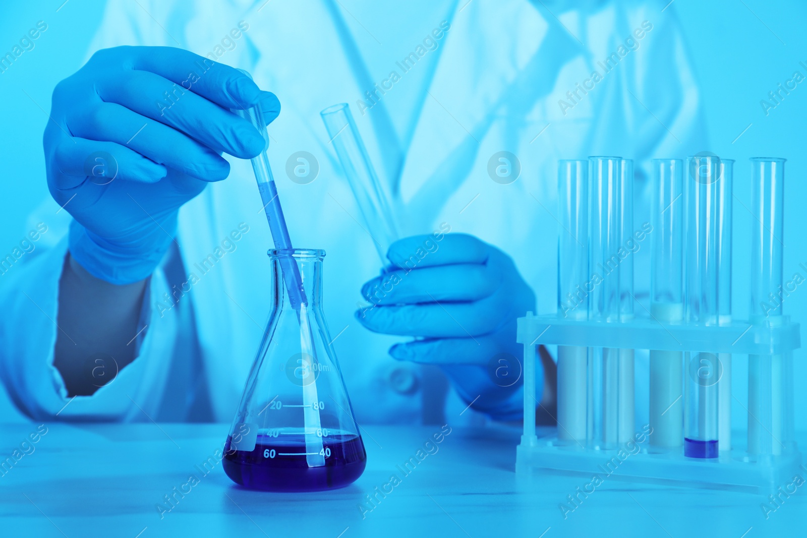 Photo of Laboratory testing. Scientist working with glassware at table, closeup. Toned in blue