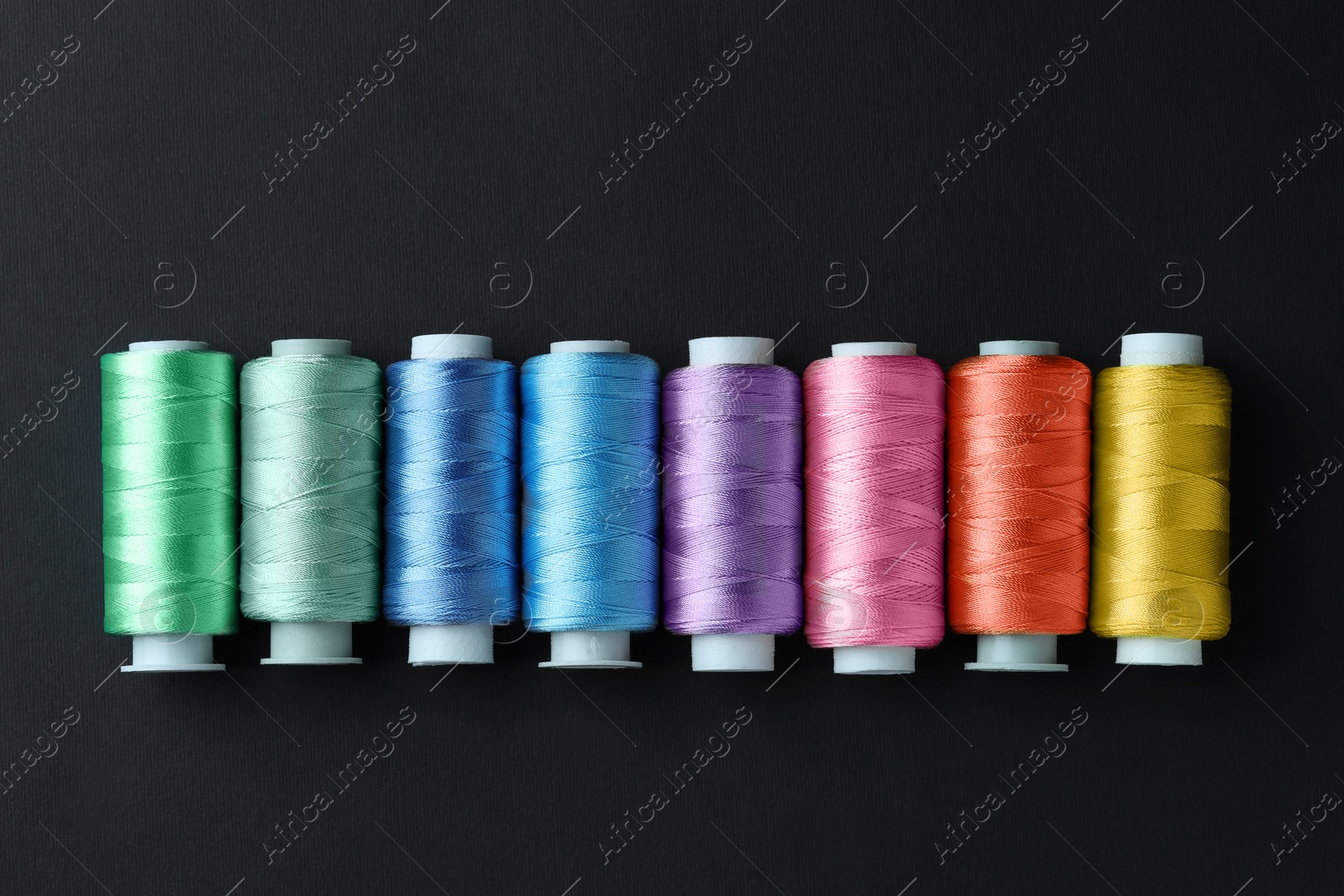 Photo of Spools of colorful sewing threads on black background, flat lay