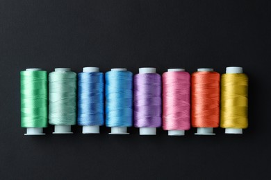 Photo of Spools of colorful sewing threads on black background, flat lay