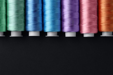 Photo of Spools of colorful sewing threads on black background, flat lay. Space for text