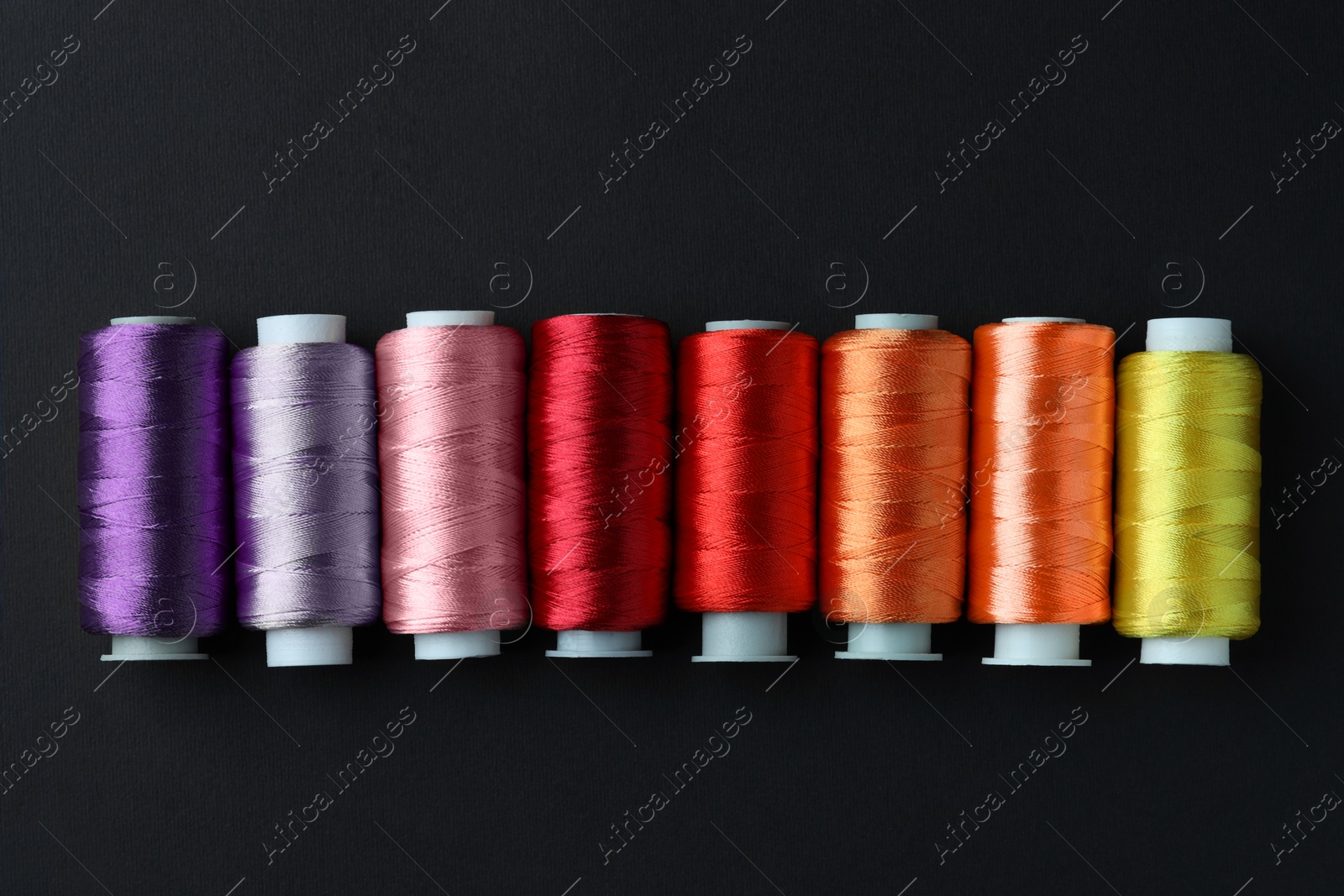 Photo of Spools of colorful sewing threads on black background, flat lay