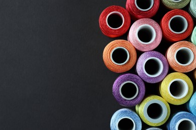 Photo of Spools of colorful sewing threads on black background, flat lay. Space for text