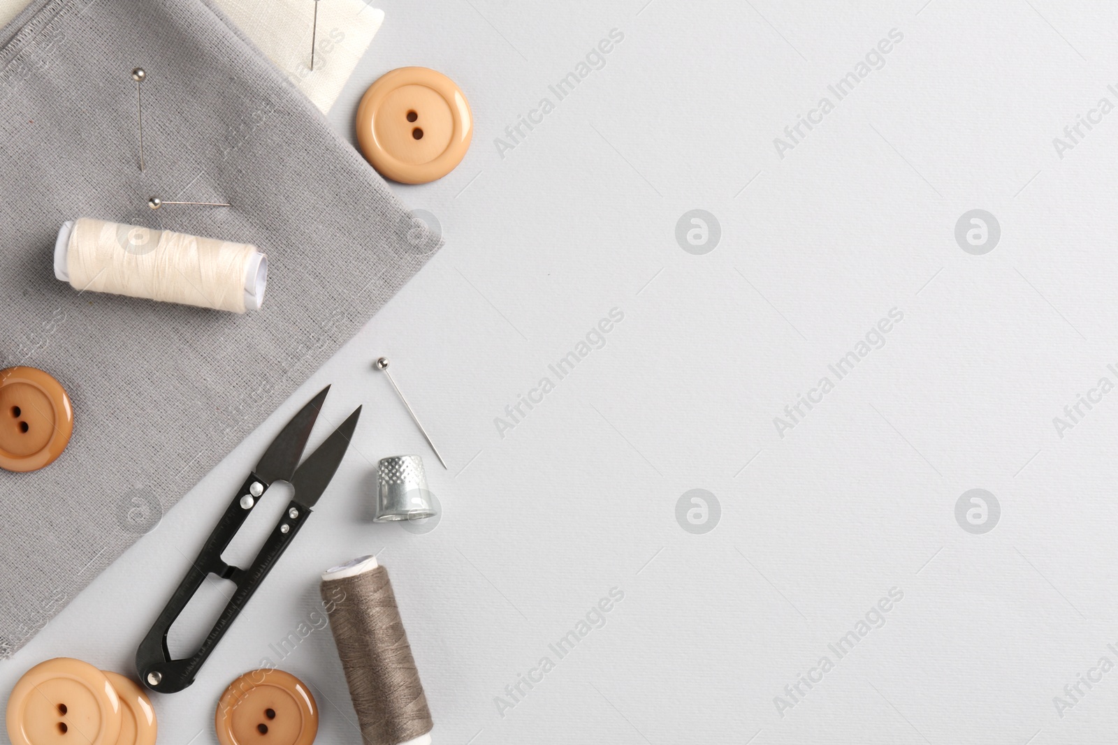 Photo of Different sewing supplies and fabric on light grey background, flat lay. Space for text