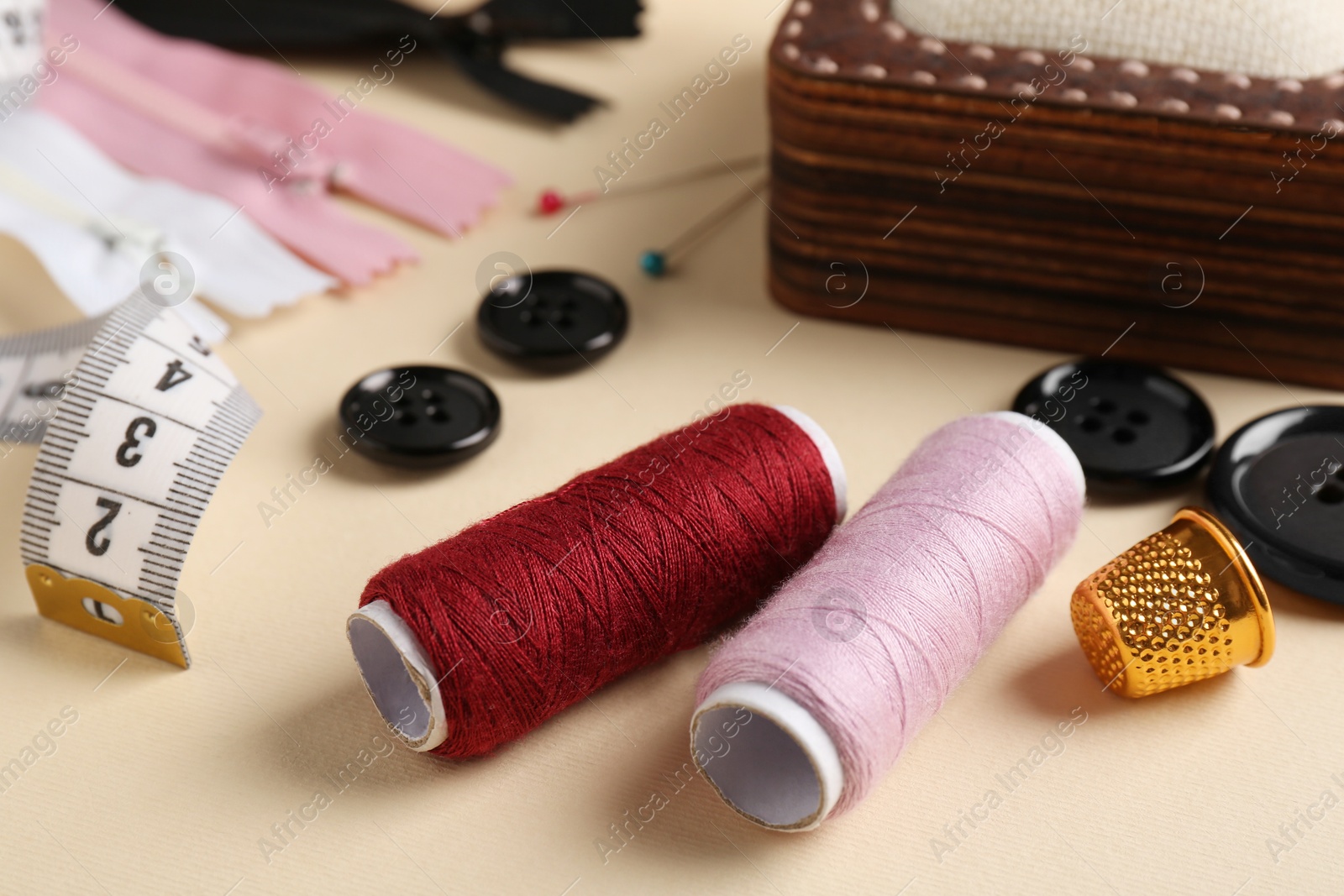 Photo of Different sewing supplies on beige background, closeup