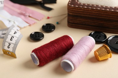 Photo of Different sewing supplies on beige background, closeup