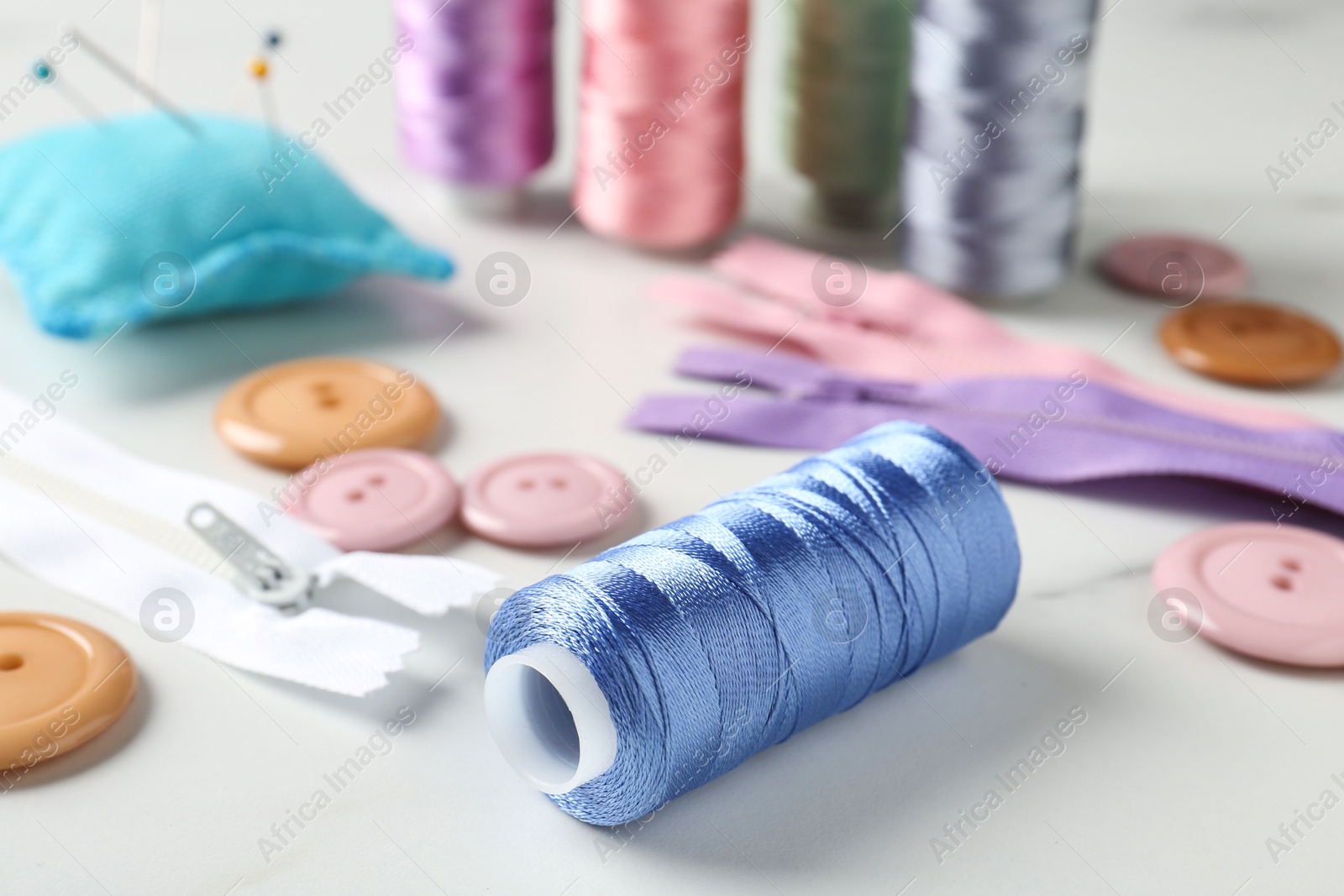 Photo of Different sewing supplies on white marble table, closeup