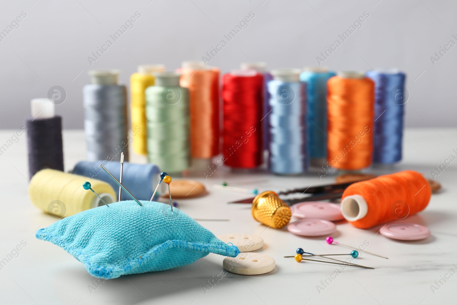 Photo of Different sewing supplies on white marble table, closeup