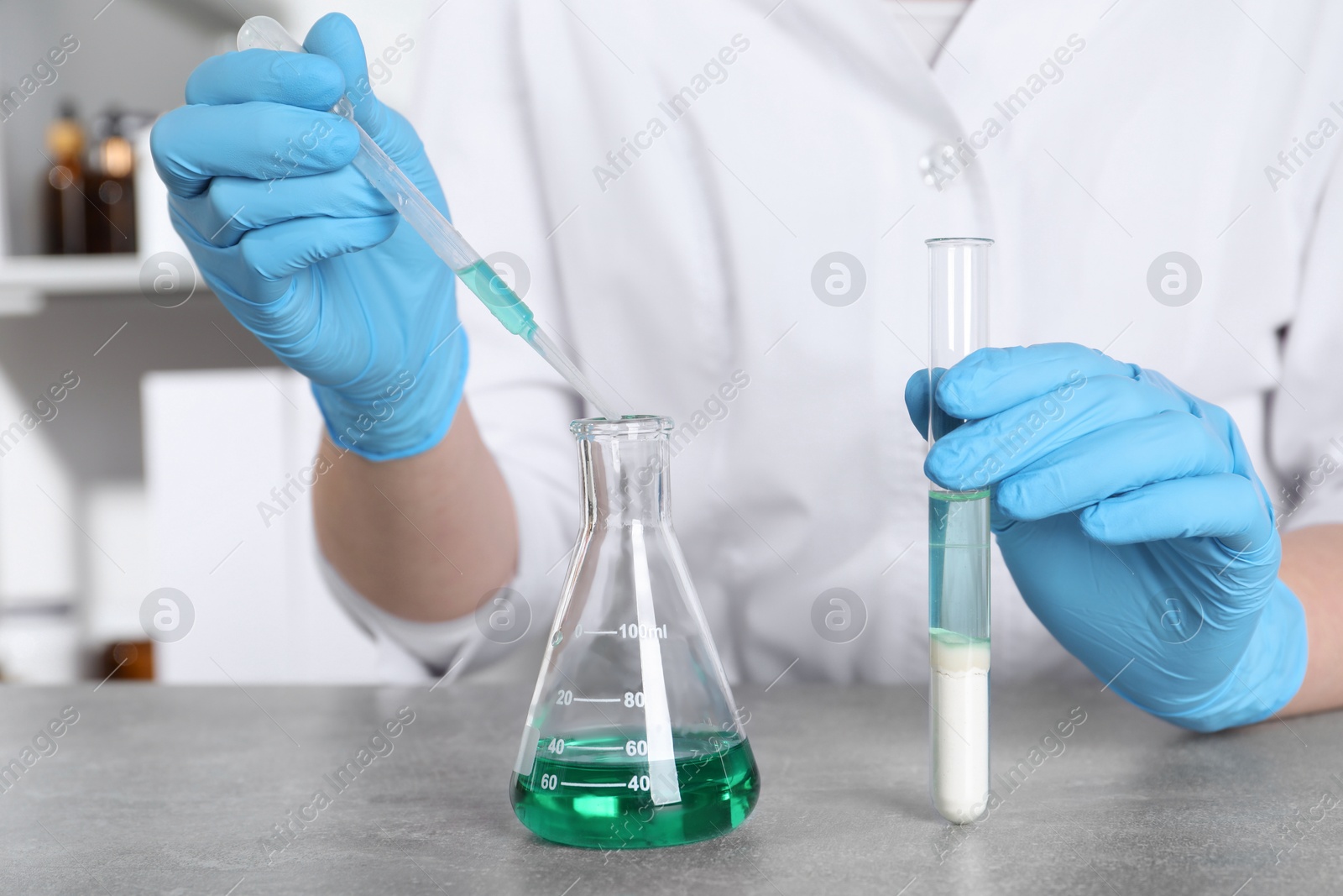 Photo of Laboratory testing. Scientist with test tube taking sample from flask at grey table indoors, closeup