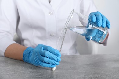 Photo of Laboratory testing. Scientist pouring liquid into test tube at grey table indoors, closeup