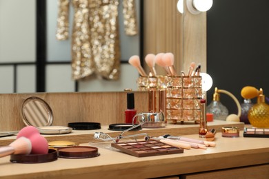 Photo of Makeup room. Mirror and cosmetic products on wooden dressing table indoors, closeup