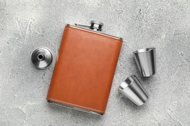 Hip flask, cups and funnel on grey textured table, flat lay