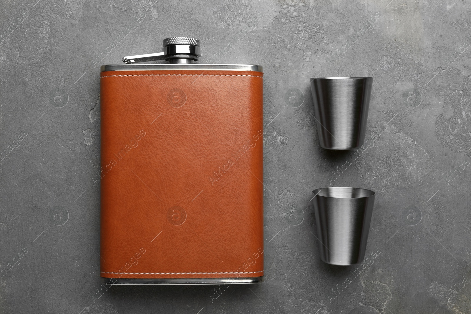 Photo of Hip flask and cups on grey table, flat lay