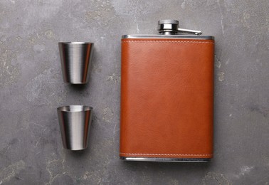 Photo of Hip flask and cups on grey table, flat lay