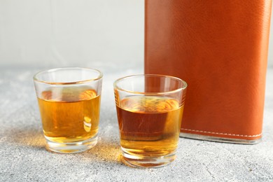 Hip flask and glasses with whiskey on grey table, closeup