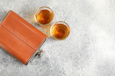 Hip flask and glasses with whiskey on grey table, flat lay. Space for text