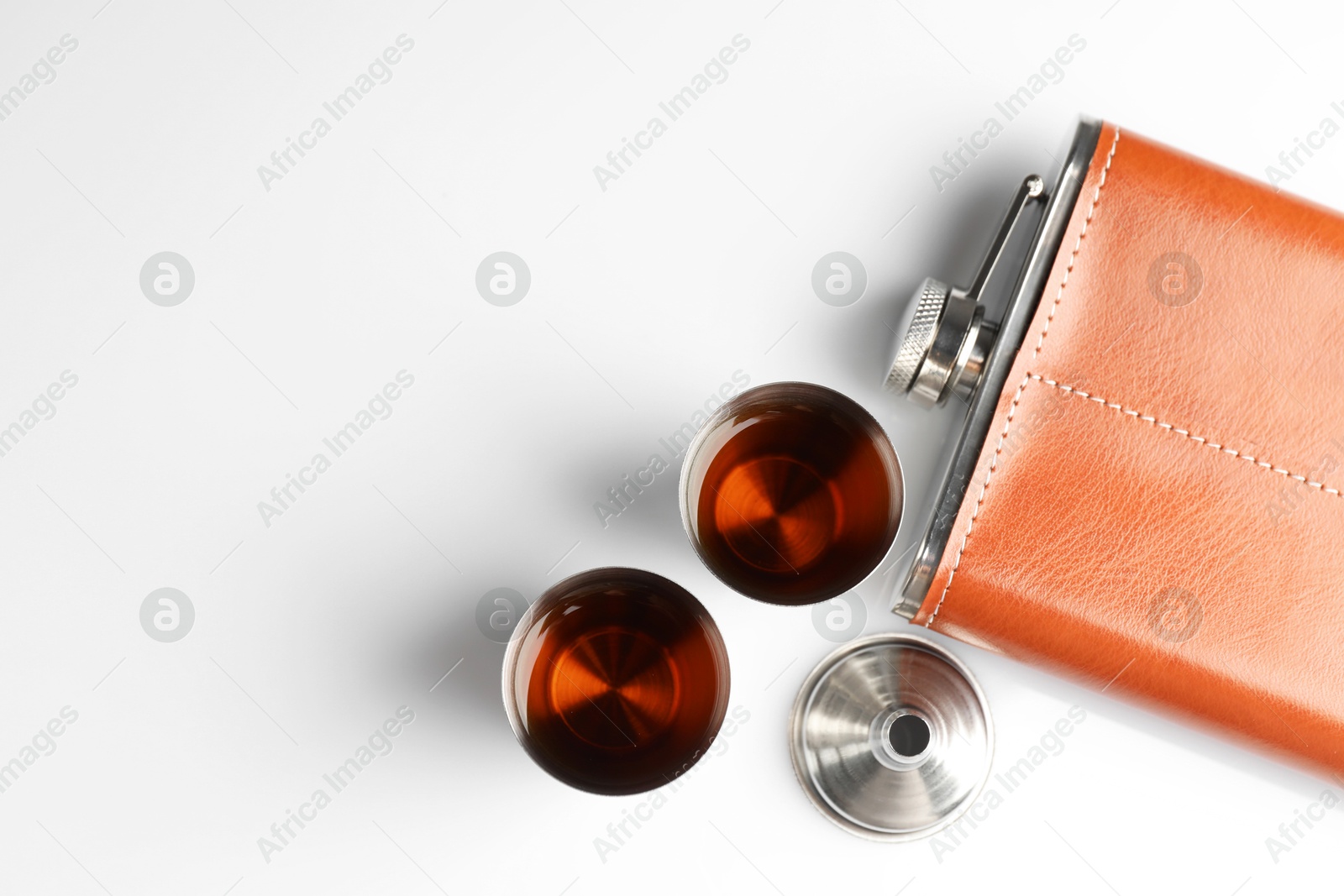 Photo of Hip flask, funnel and cups with whiskey on white table, flat lay. Space for text