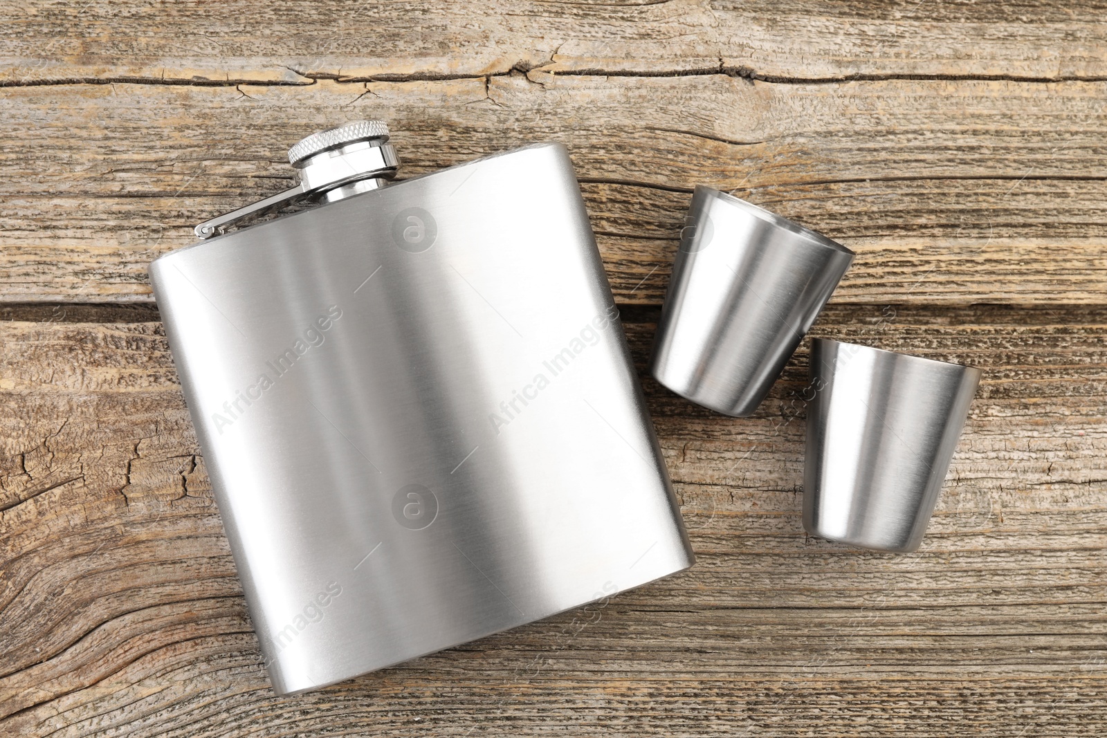 Photo of Hip flask and cups on wooden table, flat lay