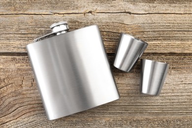 Photo of Hip flask and cups on wooden table, flat lay