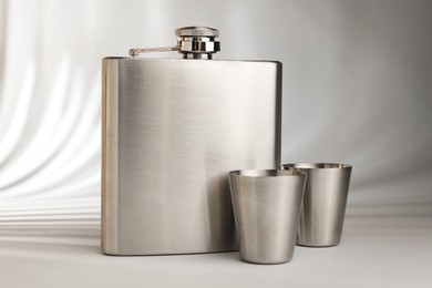 Hip flask and cups on light table, closeup