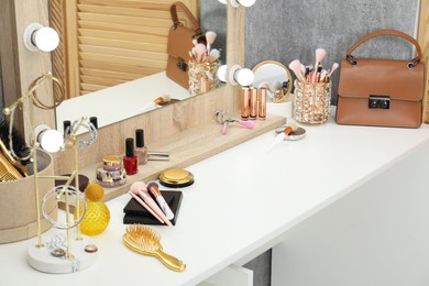 Photo of Makeup room. Mirror, different beauty products, jewelry and bag on white dressing table indoors