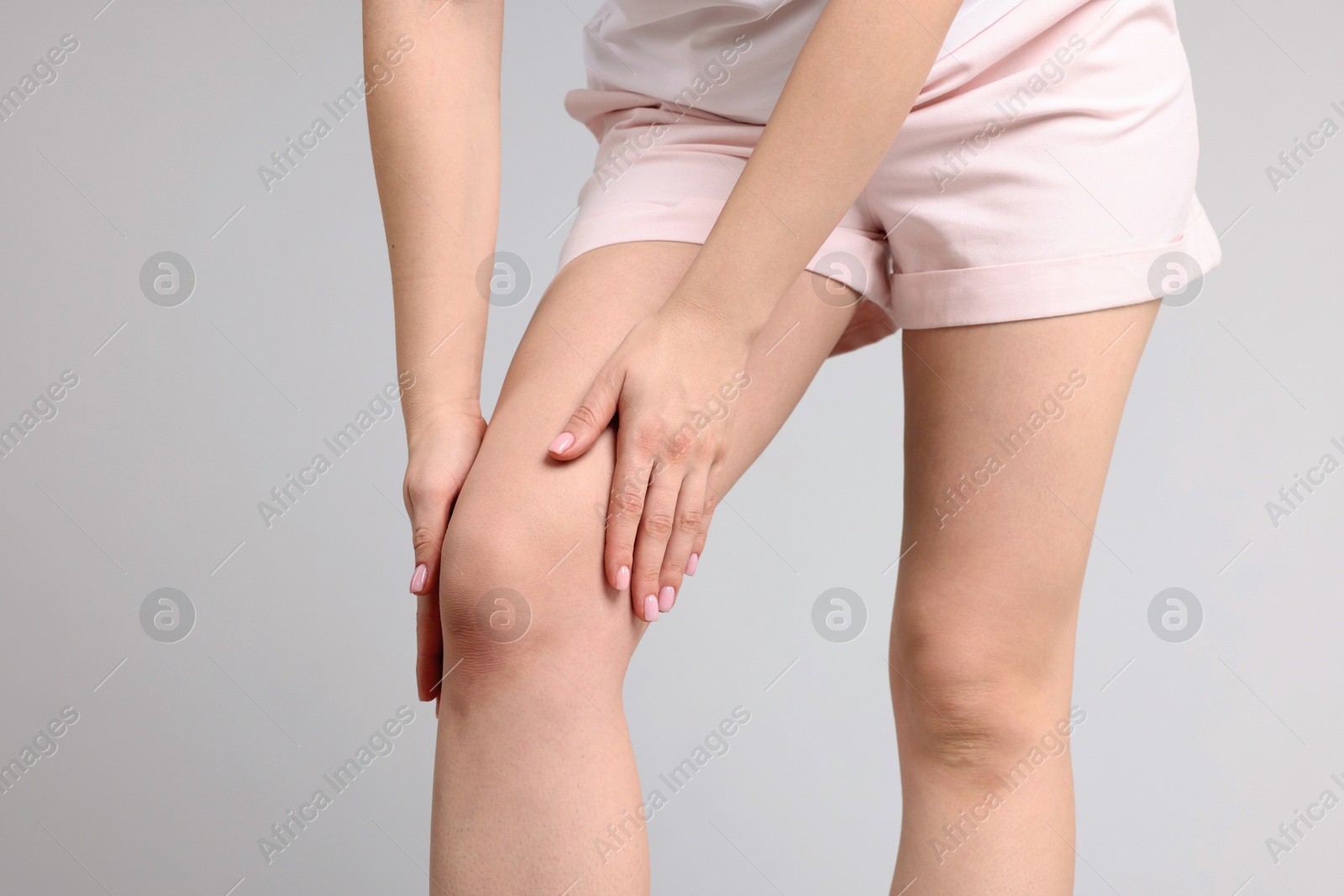 Photo of Young woman suffering from pain in knee on light grey background, closeup