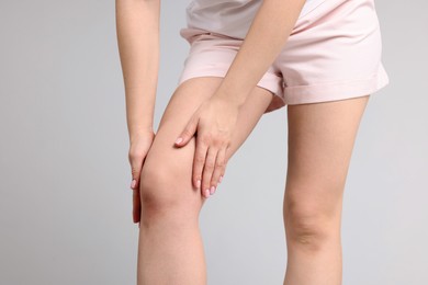 Photo of Young woman suffering from pain in knee on light grey background, closeup