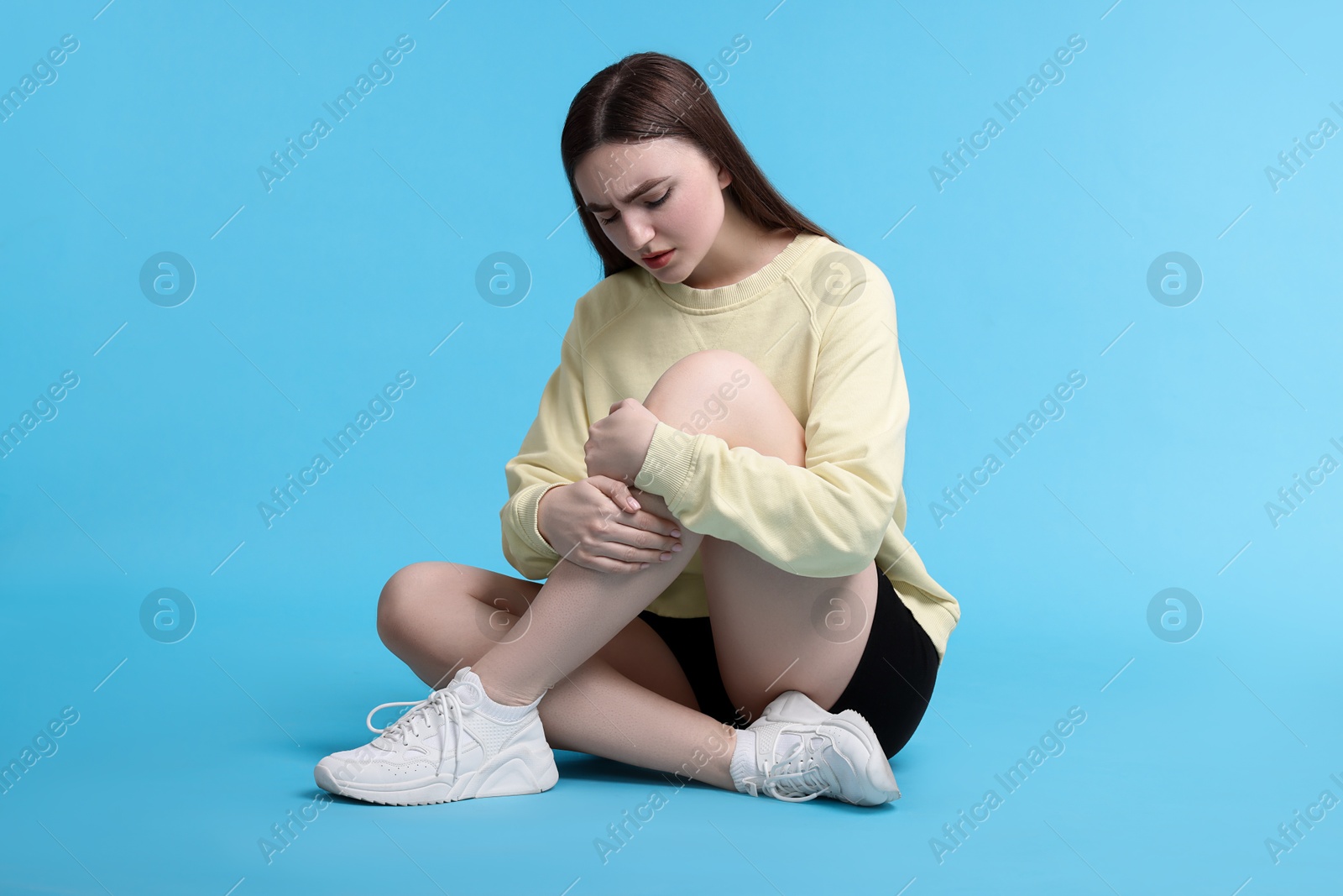 Photo of Young woman suffering from pain in knee on light blue background