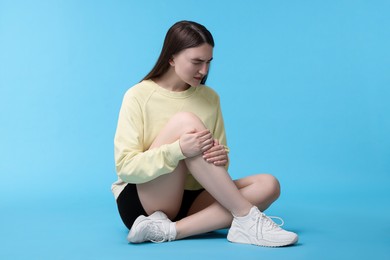 Photo of Young woman suffering from pain in knee on light blue background