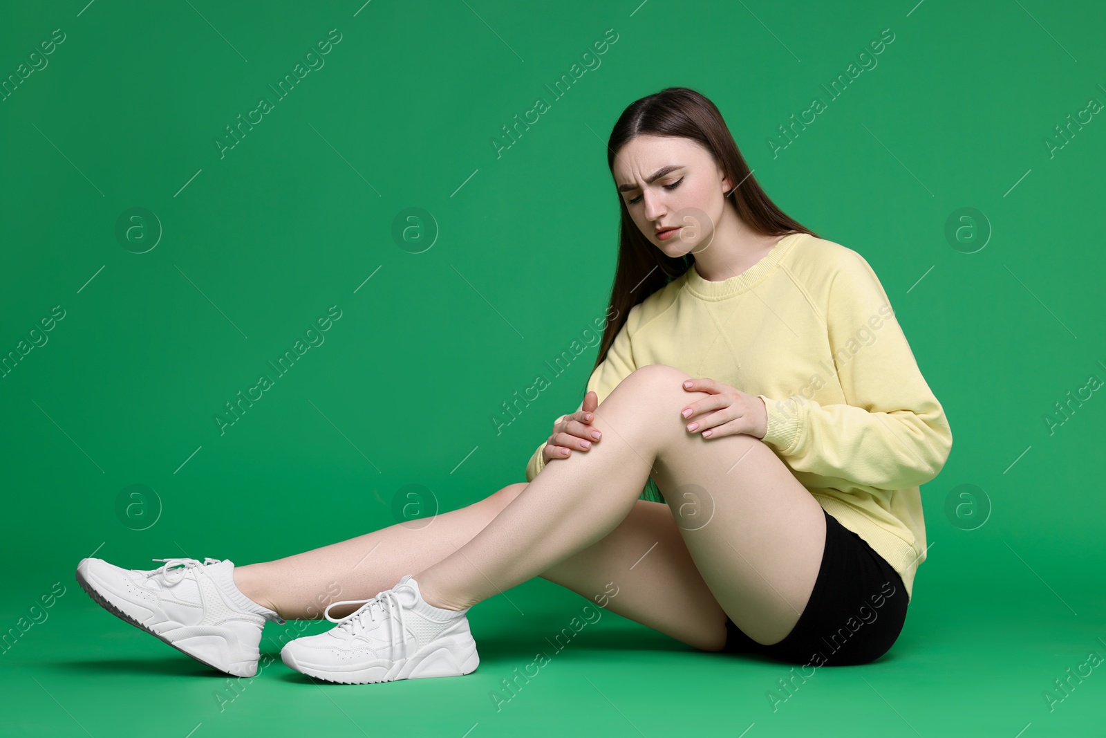 Photo of Young woman suffering from pain in knee on green background