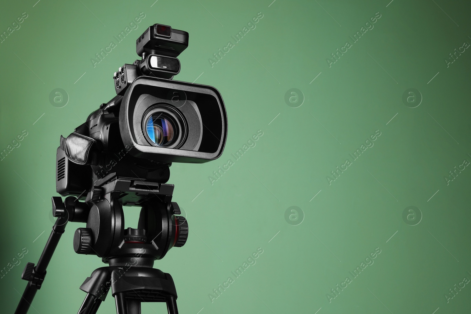 Photo of Modern professional video camera on greyish green background, space for text