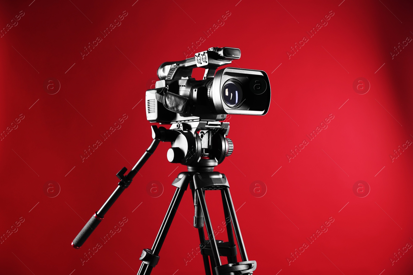 Photo of Modern video camera with tripod on red background, space for text