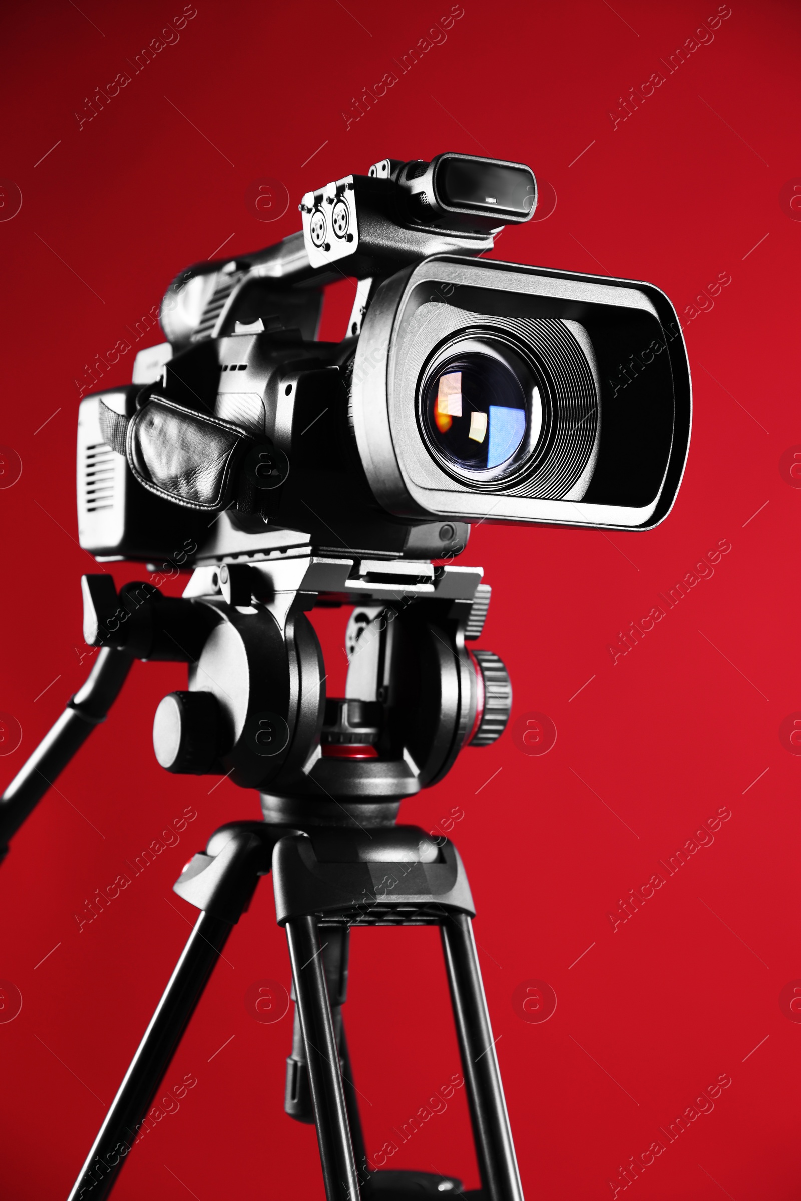 Photo of Modern video camera with tripod on red background, closeup