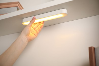 Photo of Woman putting modern LED lamp onto shelf indoors, closeup