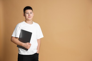 Photo of Portrait of teenage boy with laptop on beige background, space for text