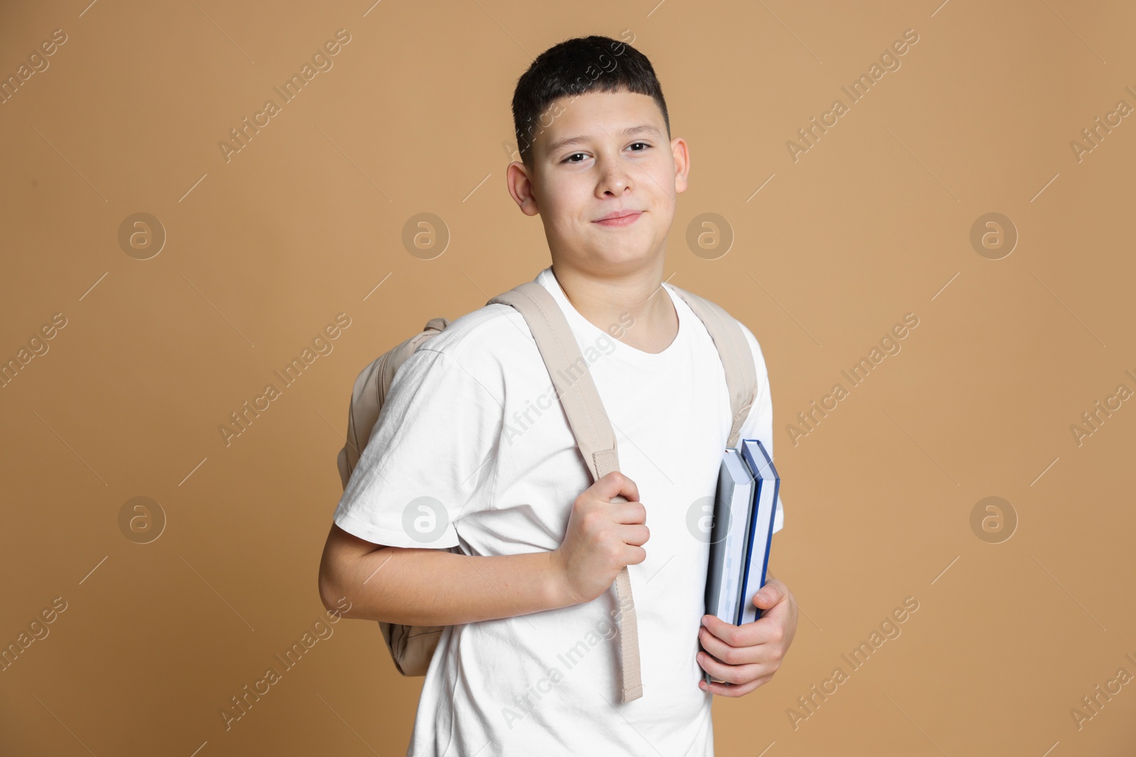 Photo of Portrait of teenage boy with books and backpack on beige background