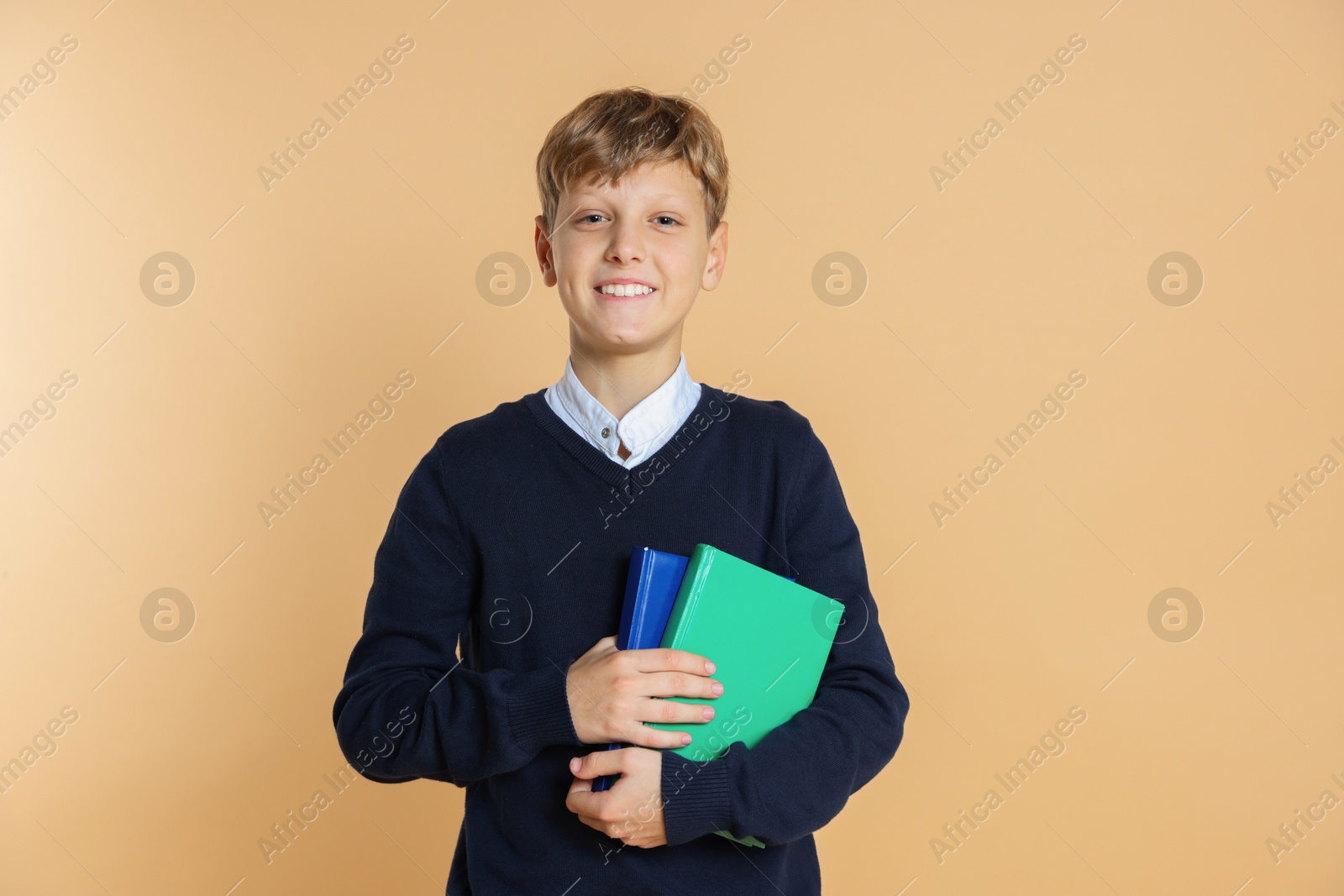 Photo of Portrait of teenage boy with books on beige background