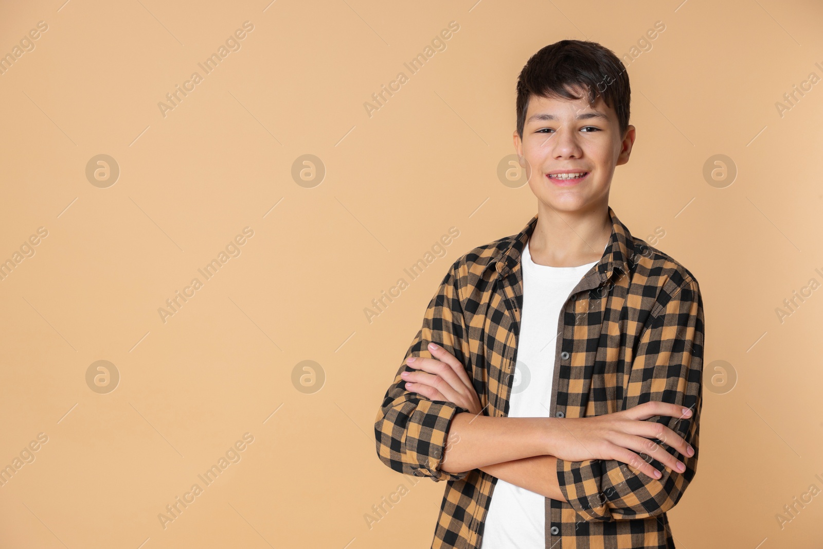 Photo of Portrait of teenage boy with crossed arms on beige background, space for text