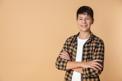 Photo of Portrait of teenage boy with crossed arms on beige background, space for text