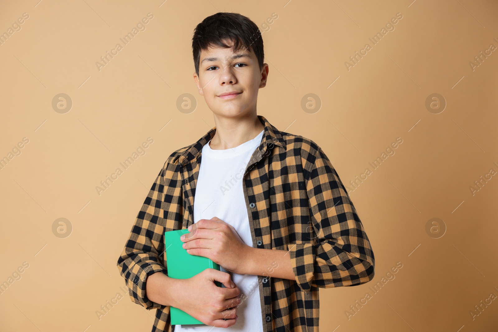 Photo of Portrait of teenage boy with books on beige background