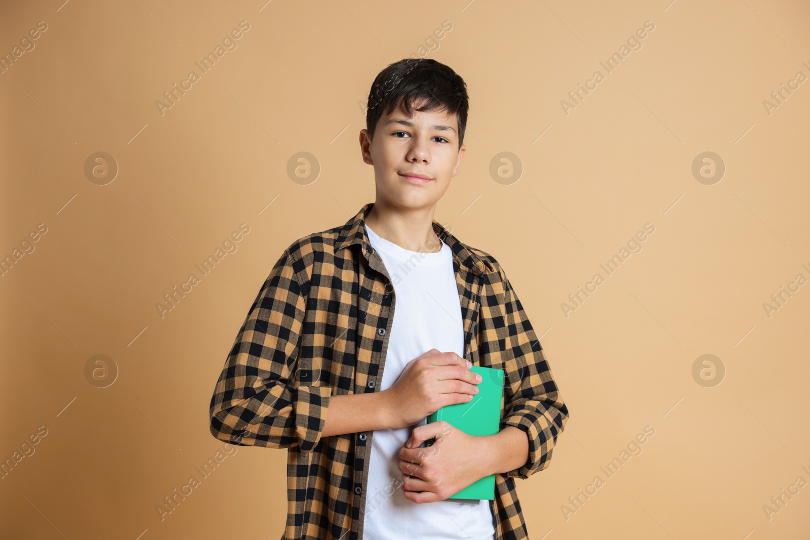 Photo of Portrait of teenage boy with books on beige background