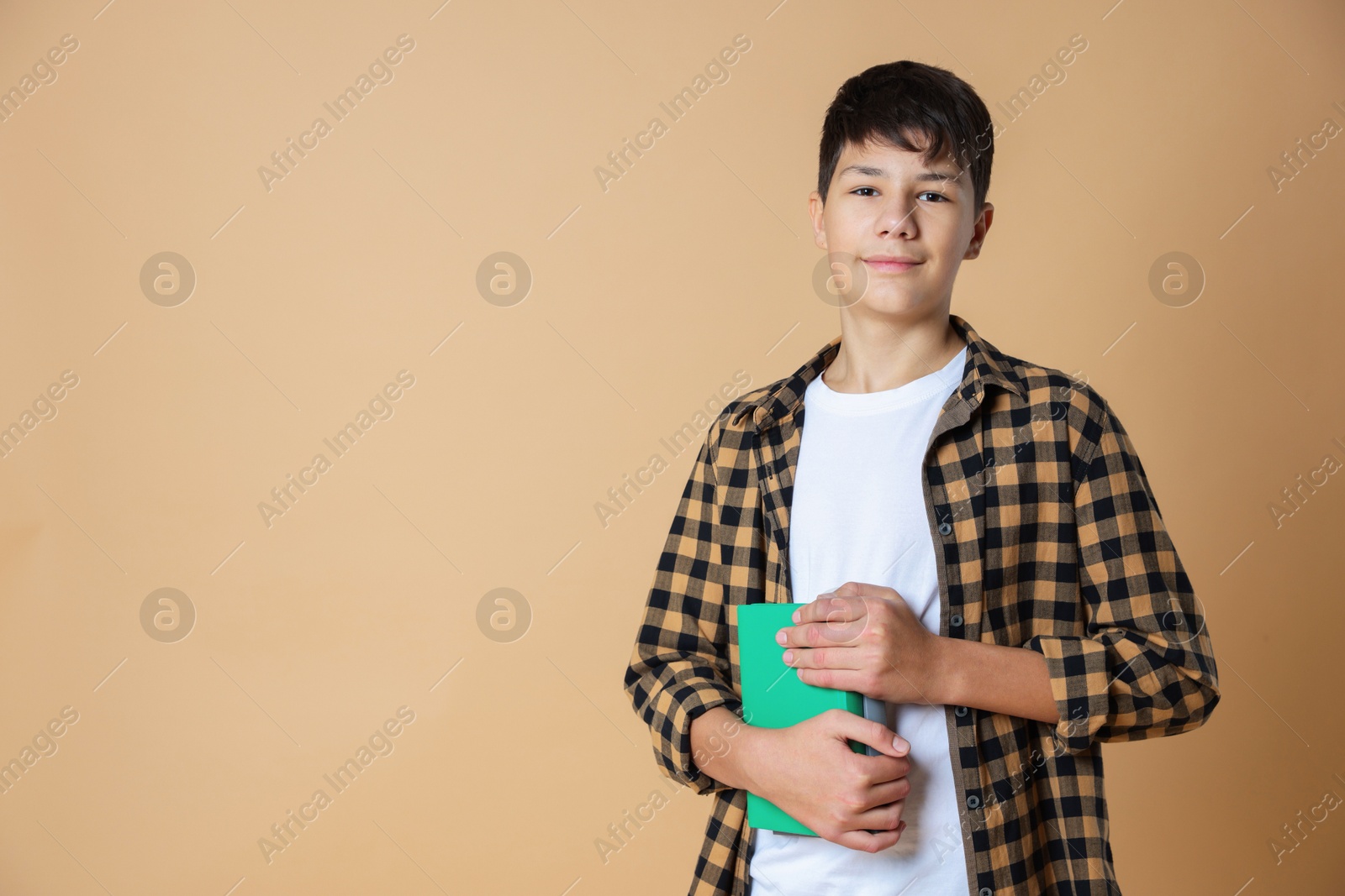 Photo of Portrait of teenage boy with books on beige background, space for text