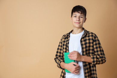 Photo of Portrait of teenage boy with books on beige background, space for text