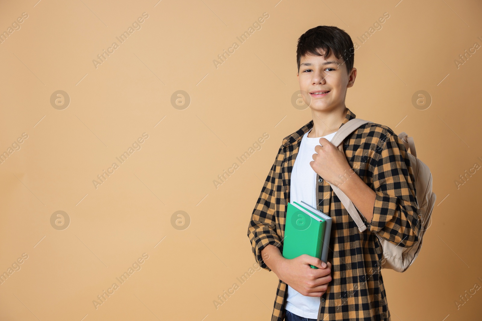 Photo of Portrait of teenage boy with books and backpack on beige background, space for text