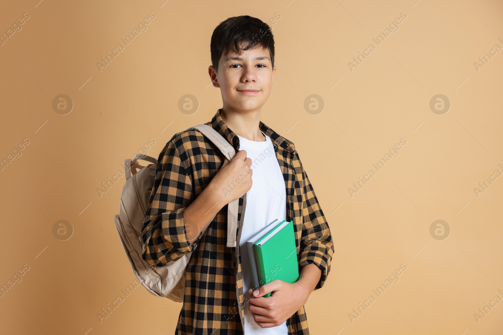 Photo of Portrait of teenage boy with books and backpack on beige background