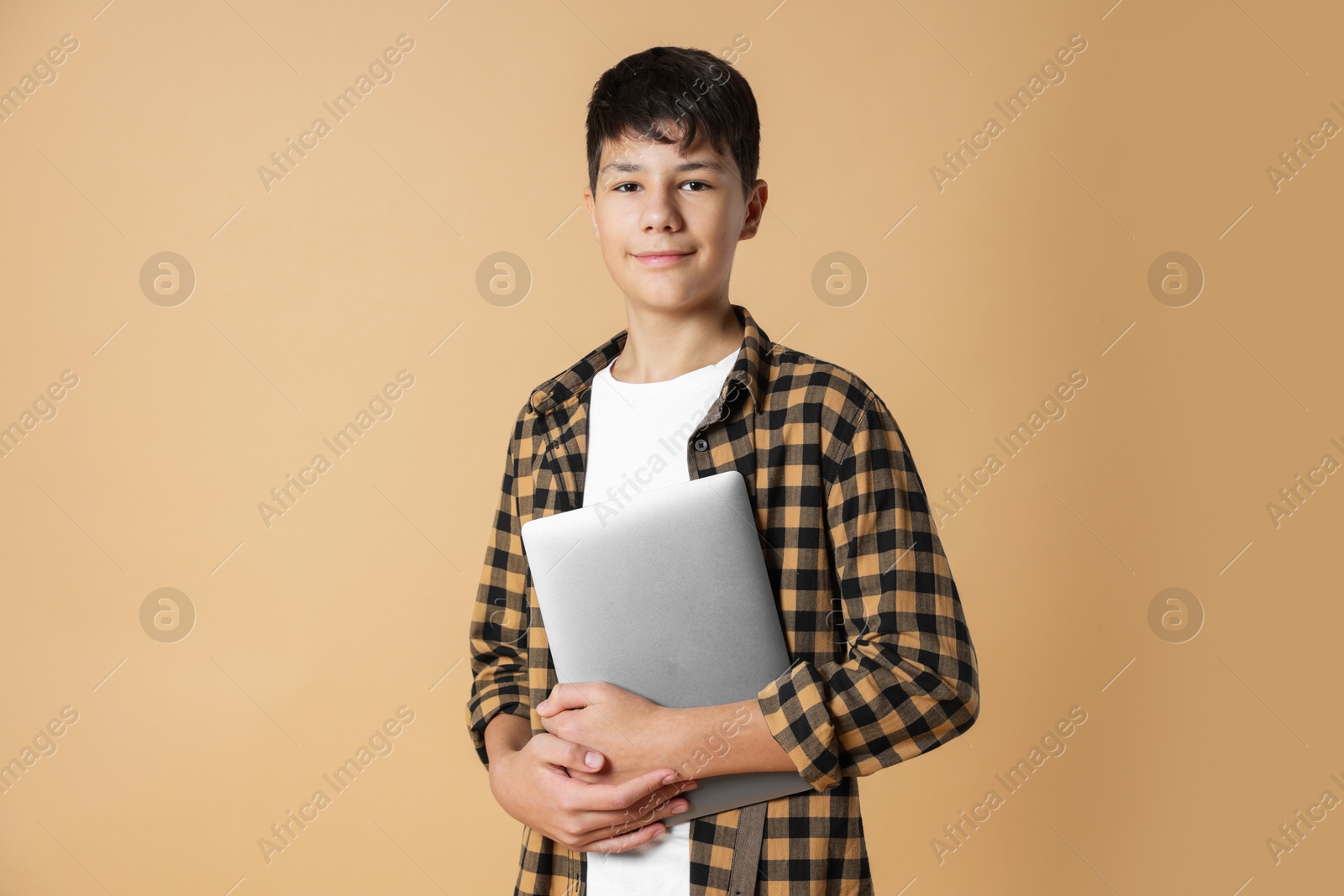 Photo of Portrait of teenage boy with laptop on beige background