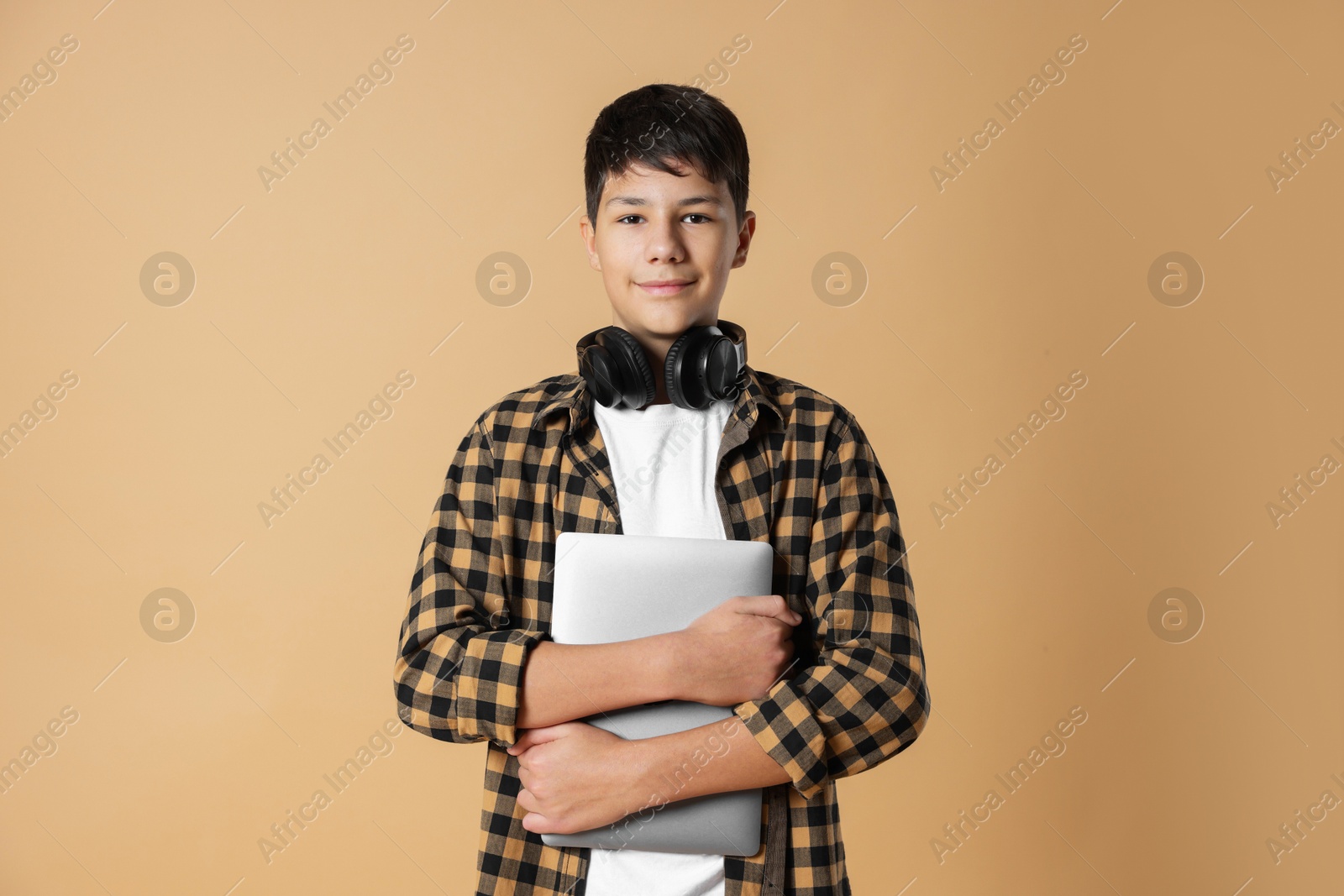 Photo of Portrait of teenage boy with laptop and headphones on beige background