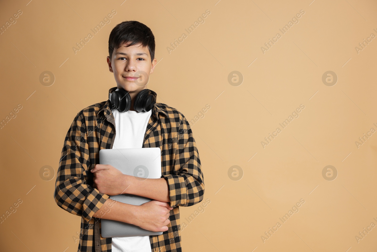 Photo of Portrait of teenage boy with laptop and headphones on beige background, space for text