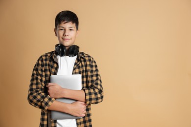 Photo of Portrait of teenage boy with laptop and headphones on beige background, space for text